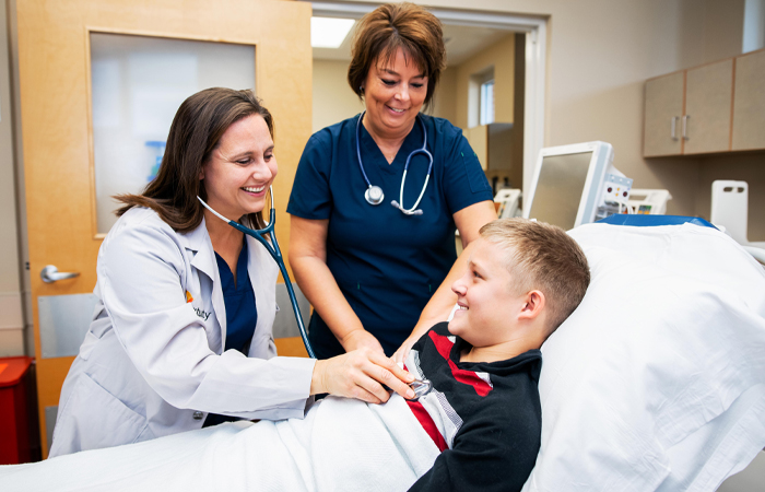 Female doctor and nurse smile as they examine male adolescent