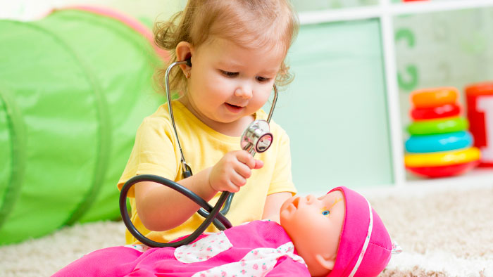 Little girl in pigtails holding stethoscope to baby doll
