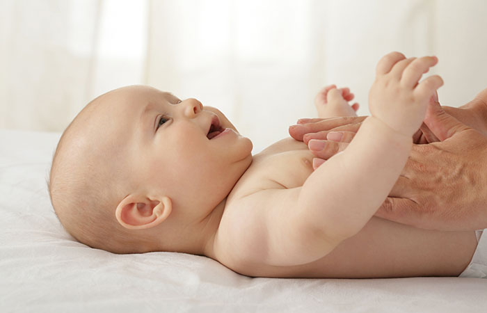 An infant smiles and lies on their back while their parent massages them