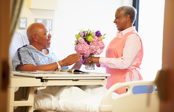 male hospital employee high fiving elderly patient laying in hospital bed