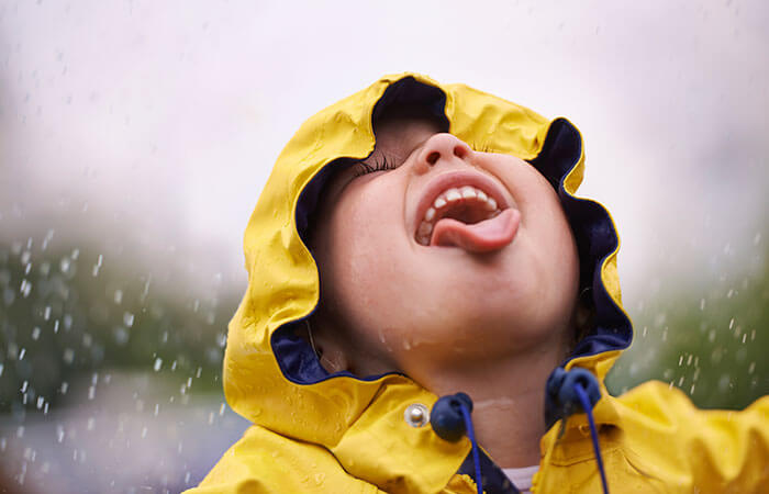 small child in a yellow raincoat tasting the rain 