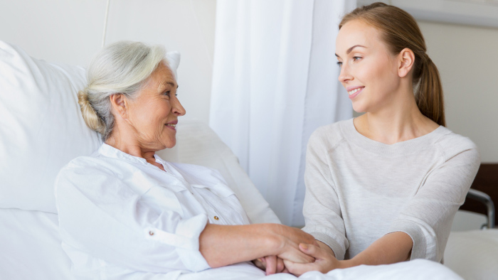 Patient in hospital bed and member of our spiritual care team hold hands