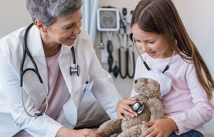young girl practicing using stethoscope on a teddy bear