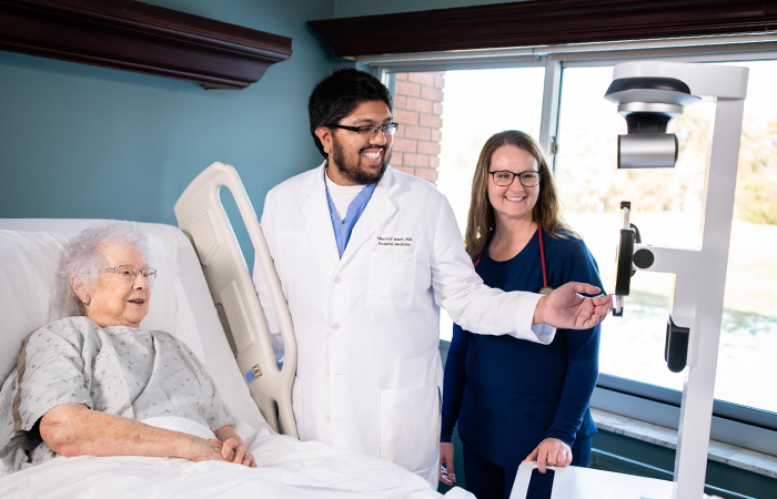 two physicians in person and one remote physician helping patient in hospital bed