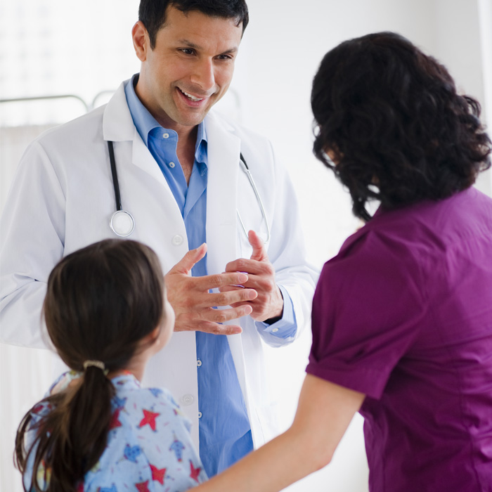 A young male doctor smiling at a female patient and her daughter