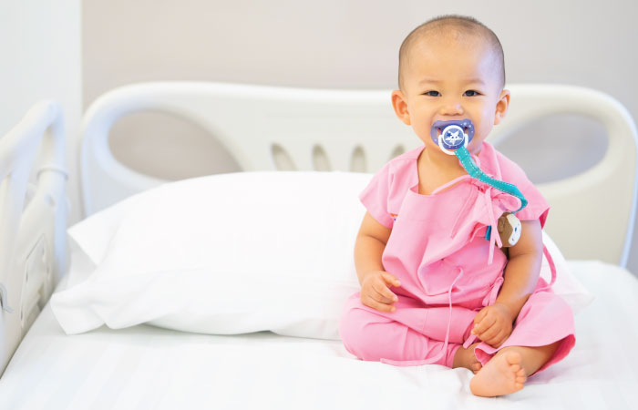 very young child sitting with pacifier in mouth on hospital bed in pink gown