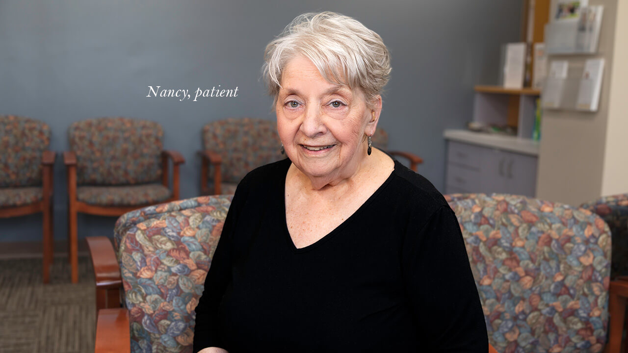 A man smiling at the camera while sitting in a garden.