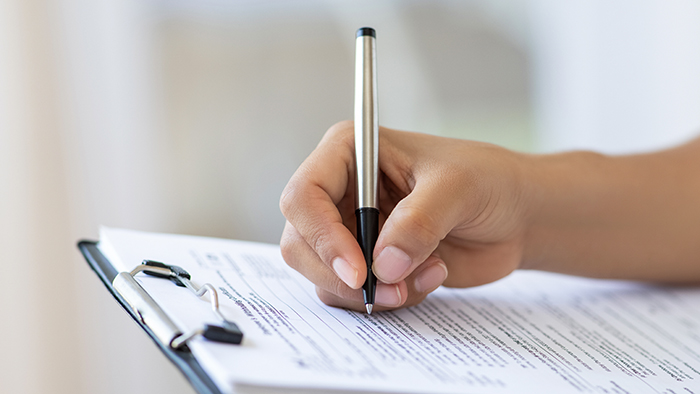 A hand writing with a pen on a clipboard