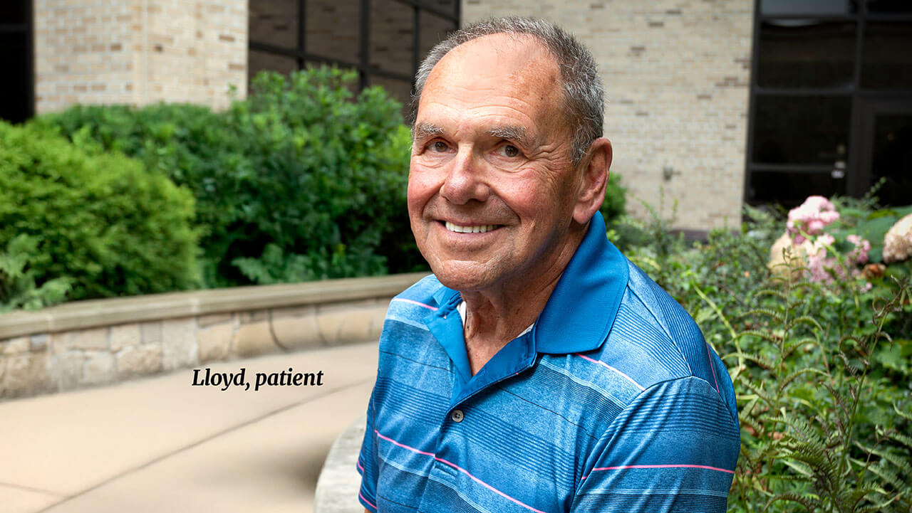 A man smiling at the camera while sitting in a garden.
