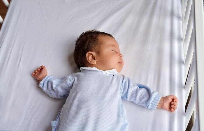 A baby wearing blue lies on its back on a hospital bed
