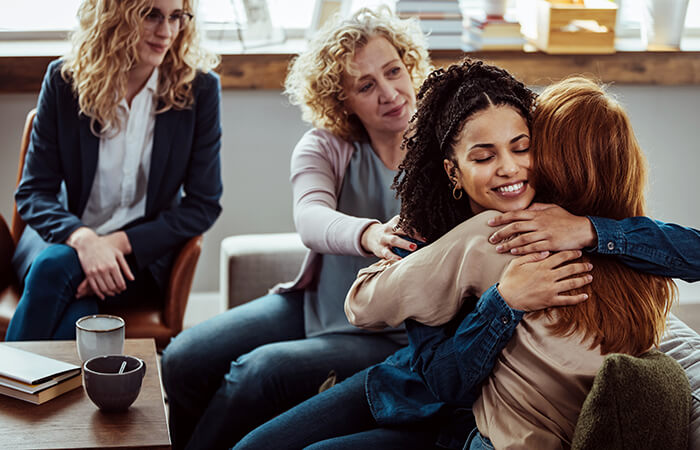 black woman and white woman hugging another white woman after sharing in a support group