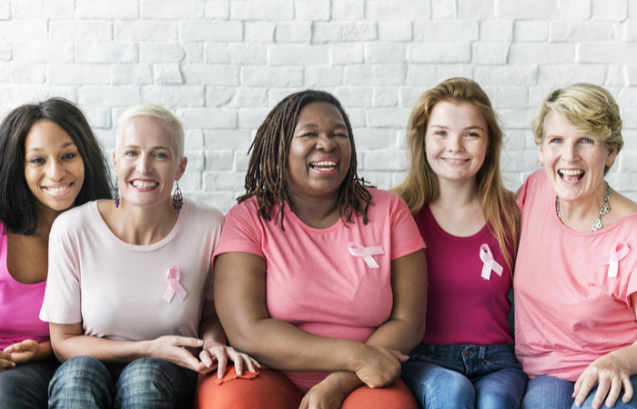 5 women sitting next to each other wearing pink shirts and breast cancer pins