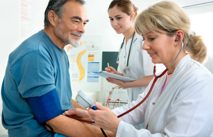 A cardiologist and a CNA giving a mature male a blood pressure screening