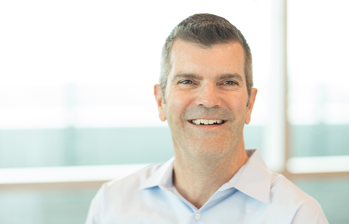 middle aged man in a hospital hallway standing and smiling at the camera 