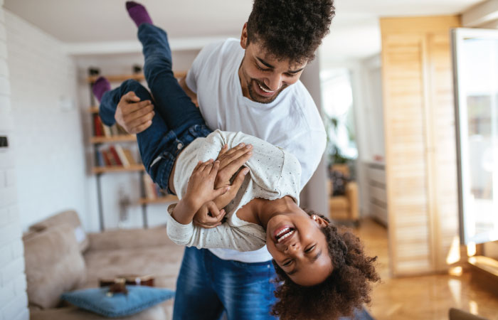 young black father holding giggling young child upside down and in the air