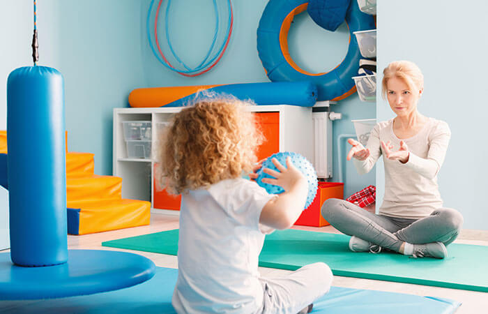 therapist and young child throwing ball back and forth 