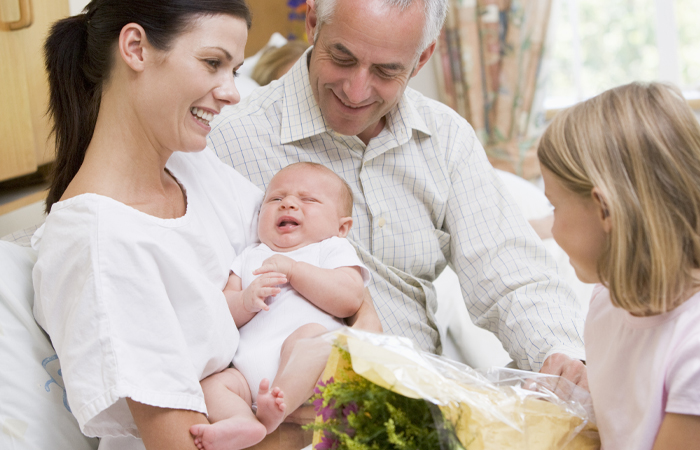 Mother holds her baby while family stands around them smiling