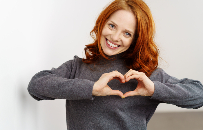 Woman smiles and makes a heart shape with her hands