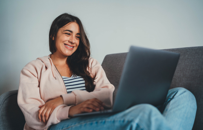Smiling female patient sitting on couch looking at laptop computer