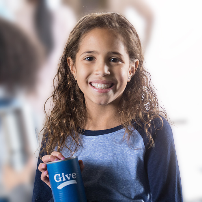 A young women in blue smiles and holds up a collection can that says Give