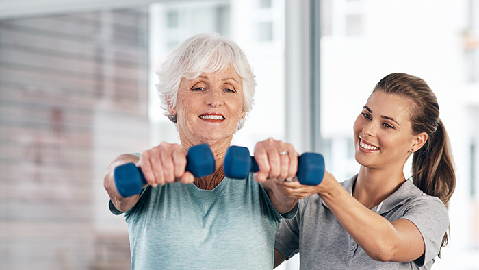 Female patient exercising with small weights with a young female physical therapist by her side