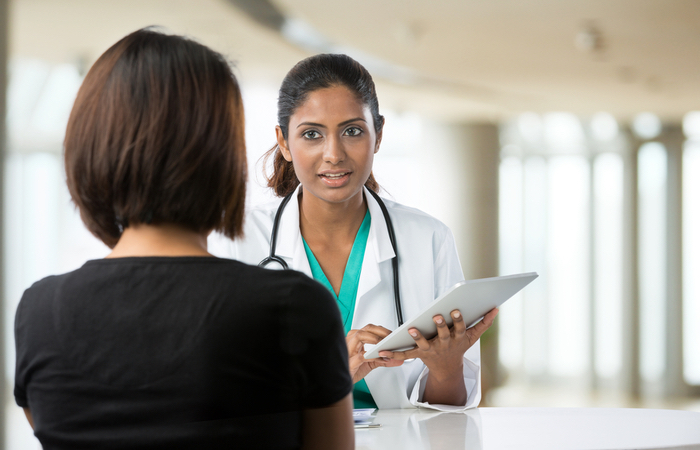 African American female provider in white coat holds a tablet as she speaks to a patient