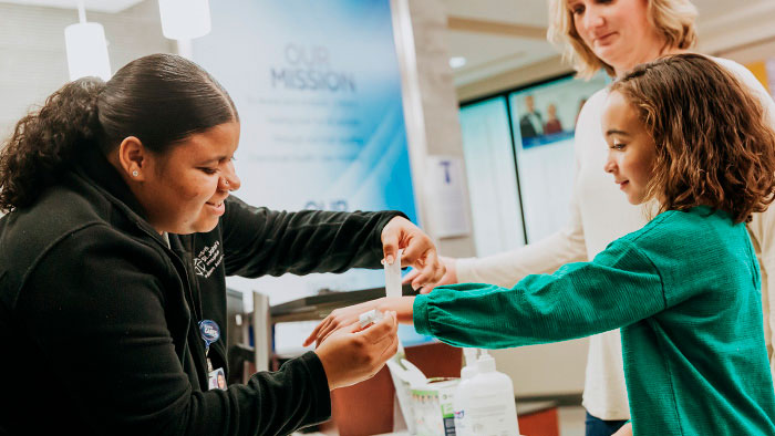 Female hospital staff puts wrist band on young patient wearing green