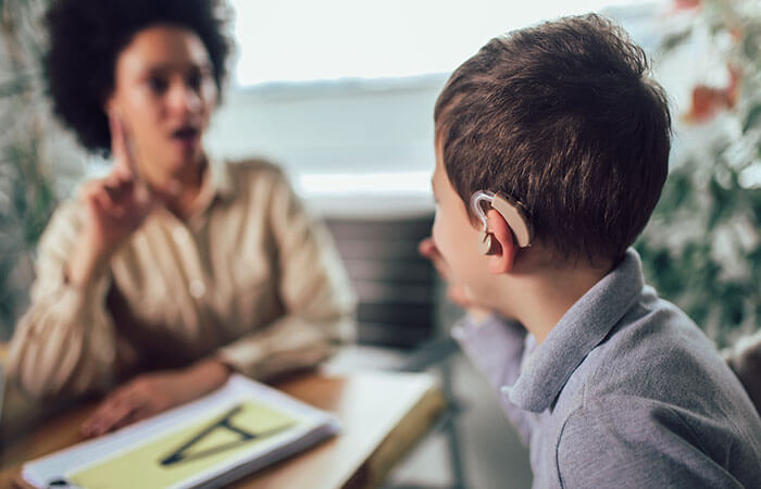 Young black audiologist doing testing with a young boy who is wearing a hearing aid in his left ear