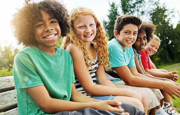 group of mixed race children smiling and sitting on a bench 