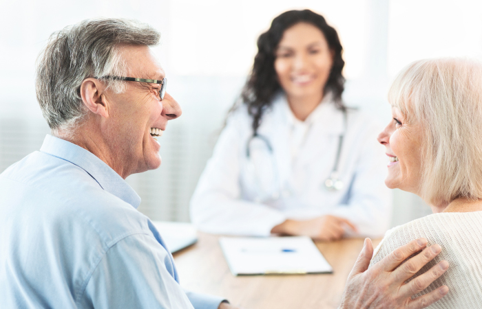 Elderly couple smiling sitting across a table from a smiling female doctor