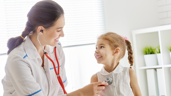 Female doctor with stethoscope checking the heart of young girl patient