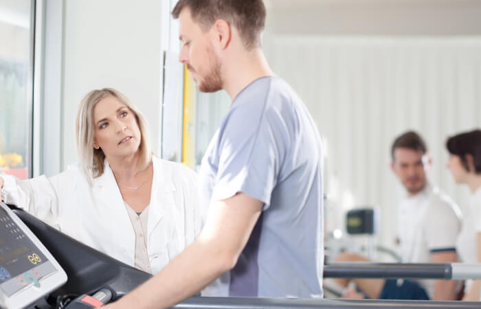 Young man walking on a treadmill while his concerned doctor monitors him.