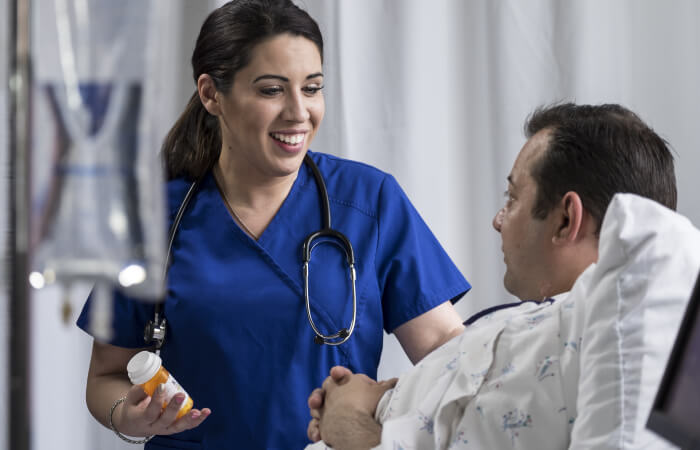 Young female nurse smiling talking bedside to a young male patient