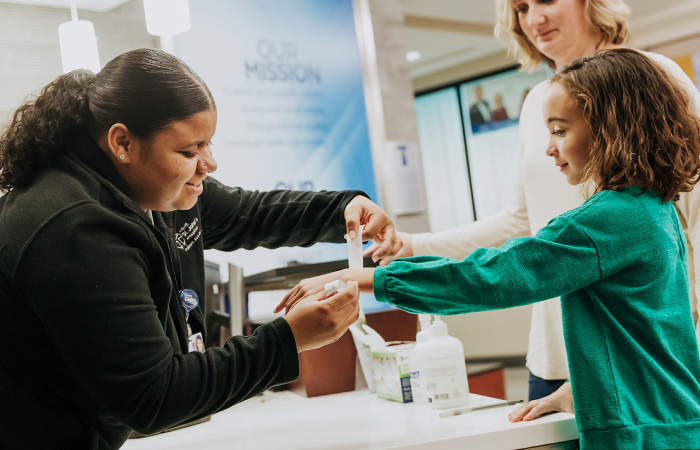 Female hospital staff puts wrist band on young patient wearing green