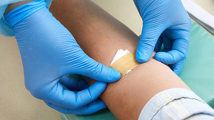 Gloved hands putting bandaid on inside elbow after blood draw