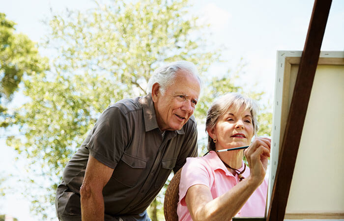 an elderly couple painting a canvas outdoors