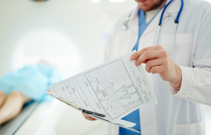 Male provider in white coat reviews patient medical records while patient is in the background