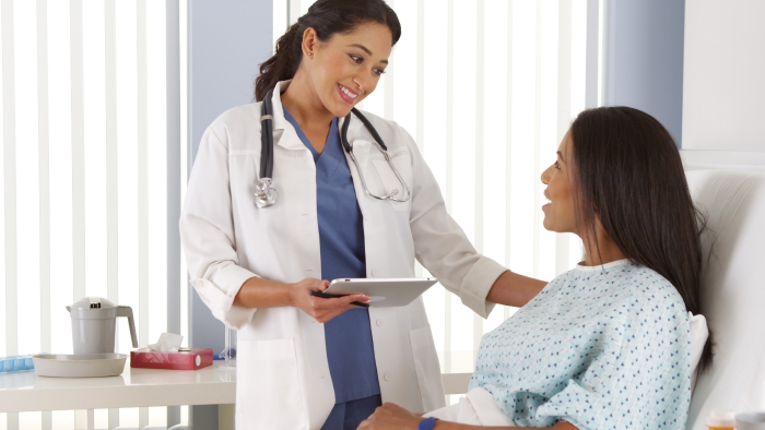 Woman doctor standing at bedside talking with woman patient