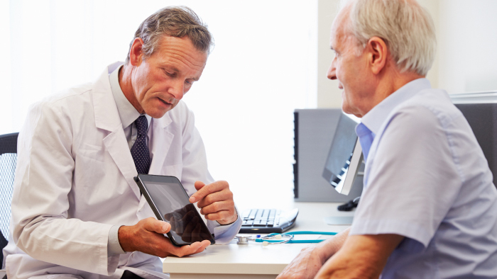 Doctor in white coat with electronic tablet talking with male patient