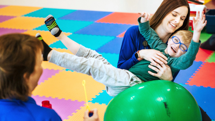 Young physical therapist playing with boy on green balance ball