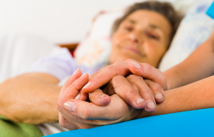 A patient is in bed with a loved one holding their hands