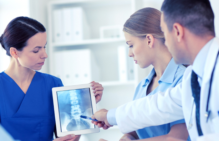 Young female nurse showing an x-ray on an iPad to a young female and male doctor