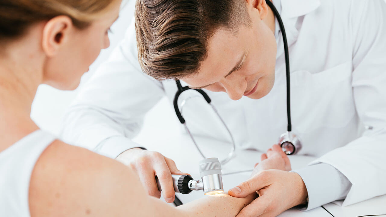 Male doctor looking at female patient's arm with a medical tool