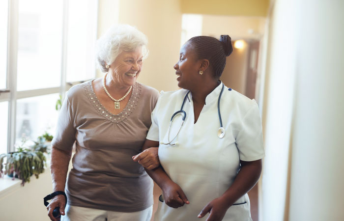 Smiling senior woman walking in arm with diverse medical professional woman