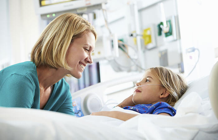 mother looking down smiling at young daughter in hospital bed in hospital room 