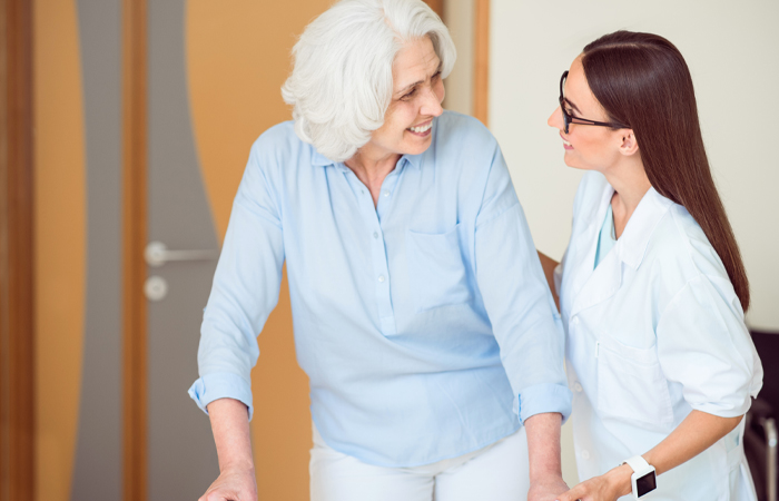 Elderly woman walking with walker next to young caretaker woman