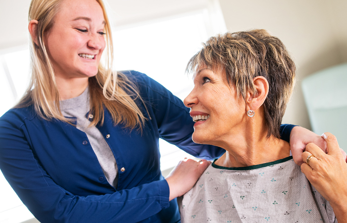 A female provider places her hands on the shoulders of a female patient.