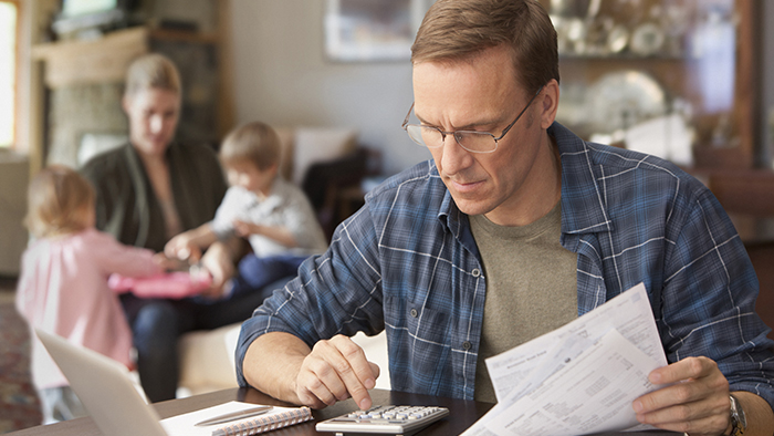 Man working on monthly bills with family in background