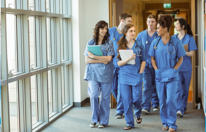 Team of nurses in blue walk down hallway in front of windows