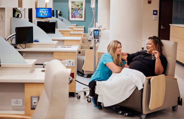 Female nurse kneeling next to woman receiving chemo in a chair